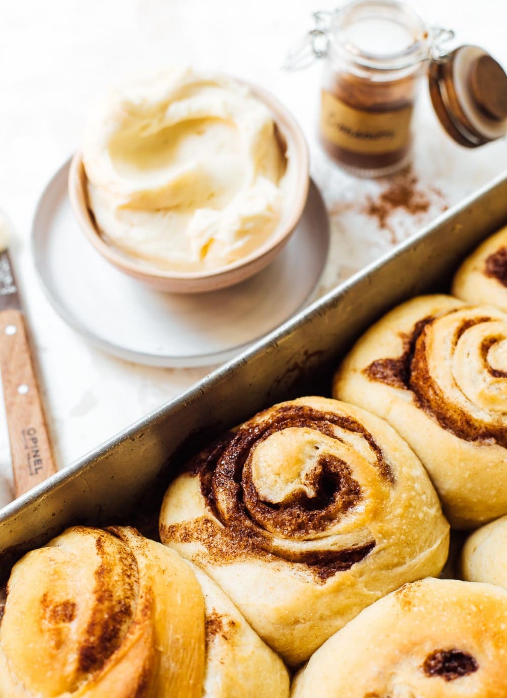 sourdough cinnamon rolls in an aluminum pan with cinnamon and cream cheese frosting next to pan