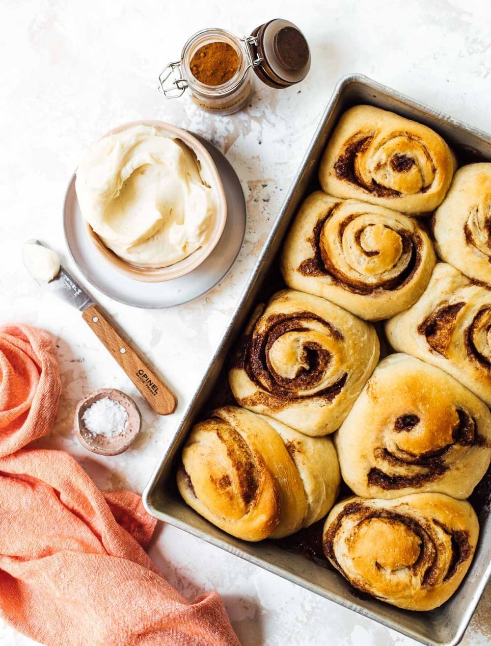 sourdough cinnamon rolls in an aluminum pan with cinnamon and cream cheese frosting next to pan