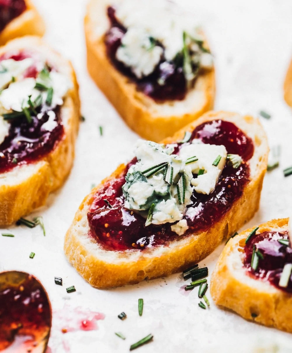 multiple crostinis with fig jam layer, then blue cheese on top and rosemary sprinkled