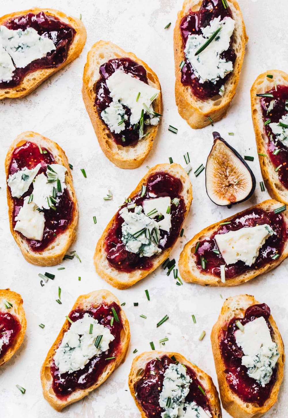 multiple crostinis with fig jam layer, then blue cheese on top and rosemary sprinkled