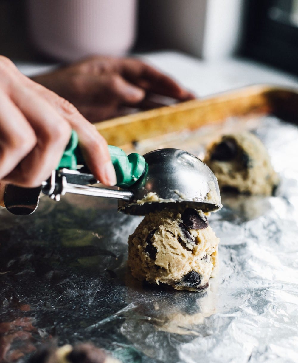 scooping cookie dough onto an aluminum foil lined cookie sheet