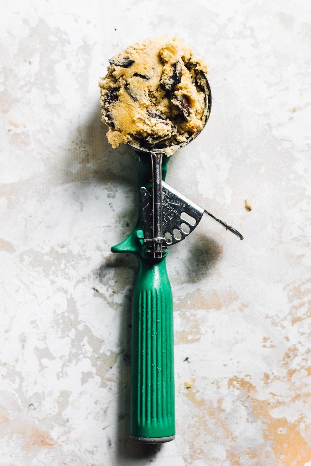 cookie scoop with a green handle that is holding chocolate chip cookie dough