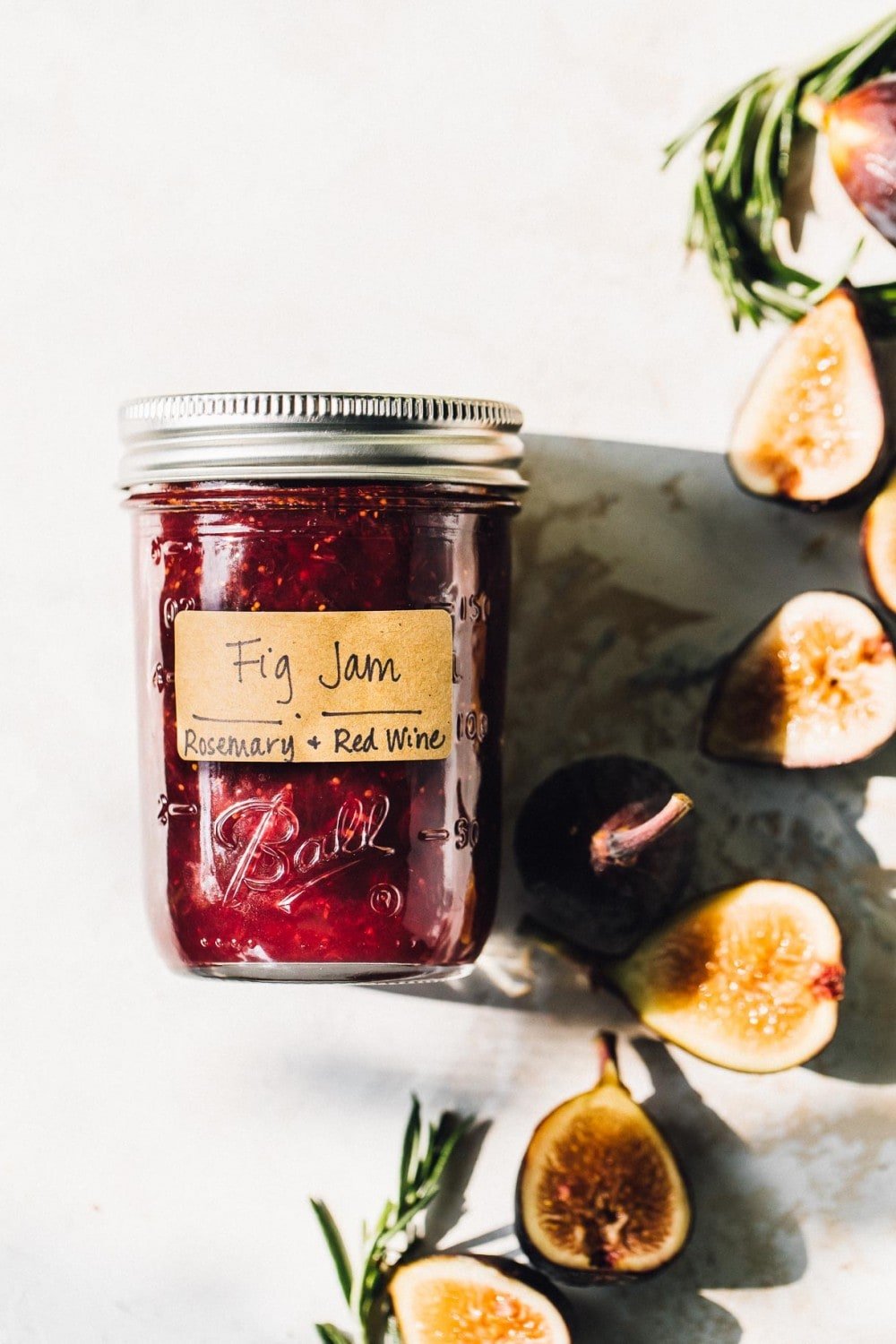 jar of fig jam in a ball jar, with craft paper label. figs and rosemary to the side of jar. 