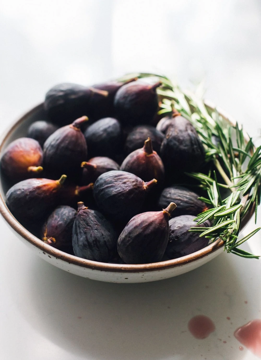 bowl of mission figs with rosemary sprigs sitting on the right side of bowl