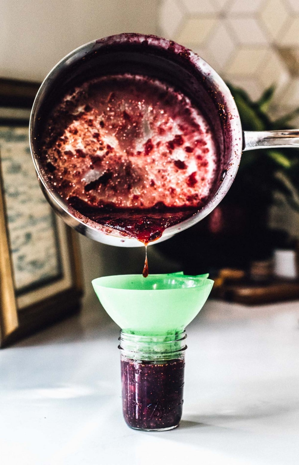 pouring fig jam into a ball canning jar, with funnel on top of jar to catch spills