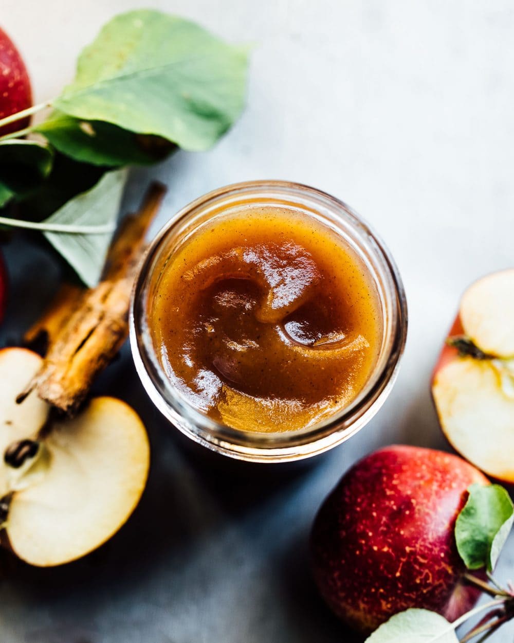 homemade apple butter in a glass jar with apples surrounding