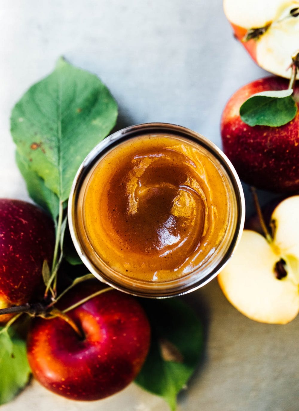 apple butter in a glass jar with top off, apples surrounding jar