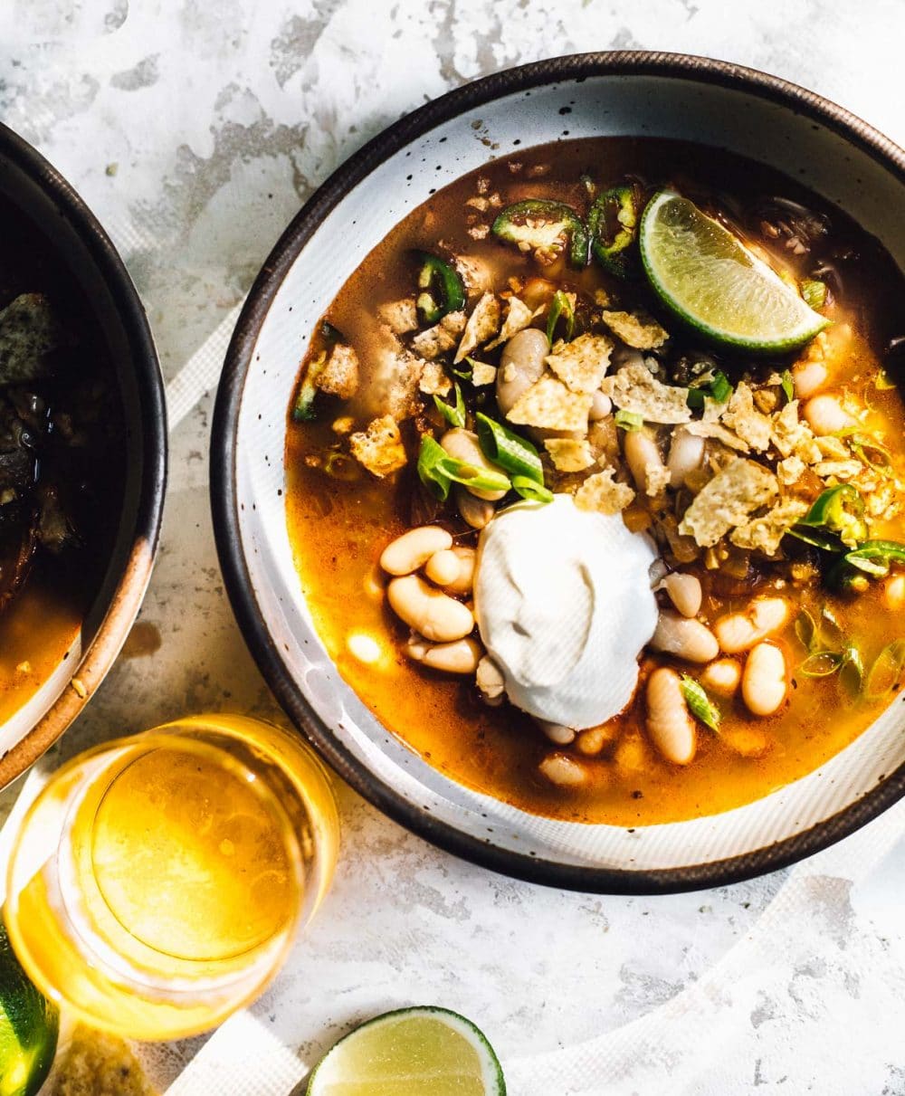 green chili soup in a white bowl, with glass of beer to bottom left