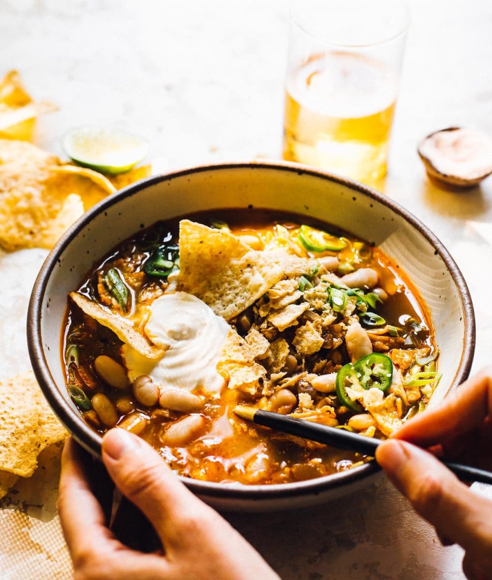 bowl of chili, woman holding the bowl, glass of beer to the right of the bowl.