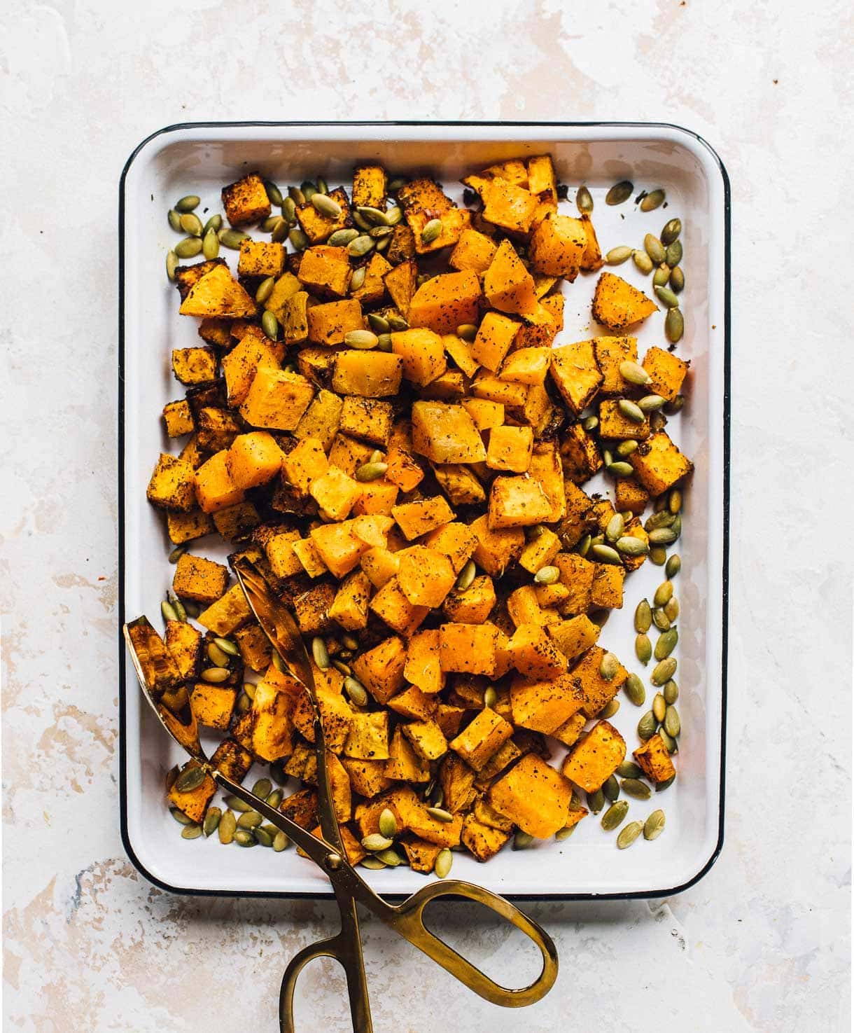 air fryer butternut squash in a white enamel pan with pepita seeds