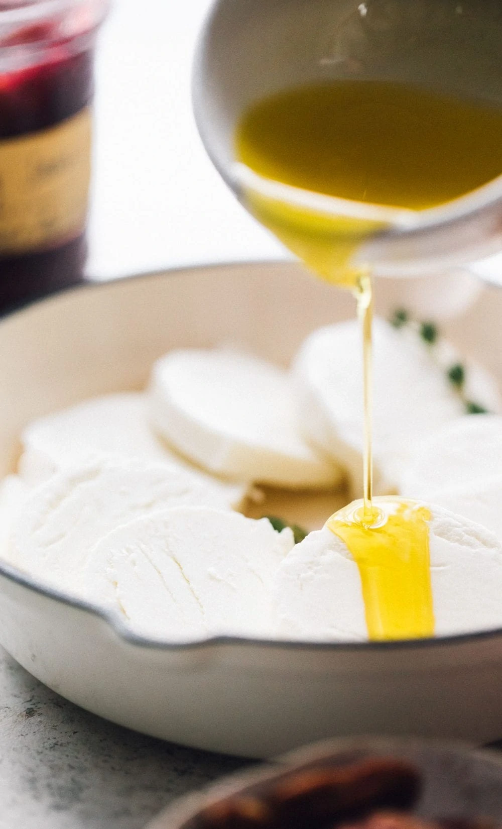 pouring olive oil over goat cheese in a white cast iron skillet
