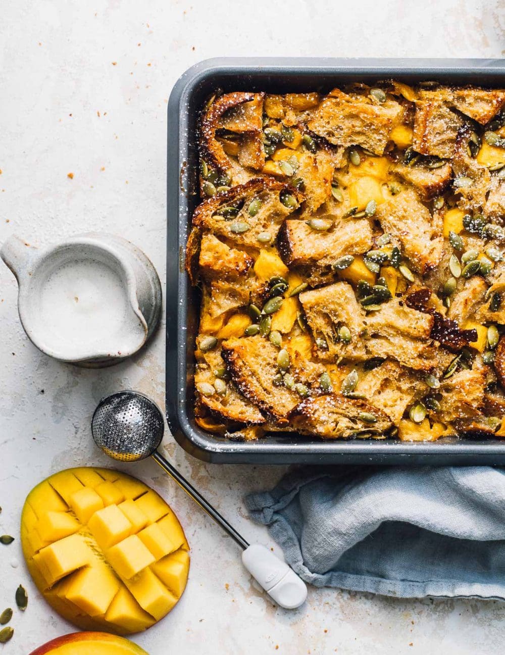 mango bread pudding in a baking pan, with cream on the right side.