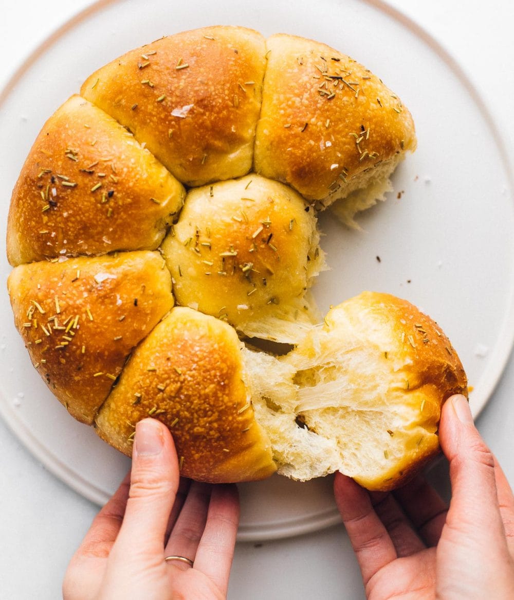 pulling sourdough dinner rolls apart, on a white plate