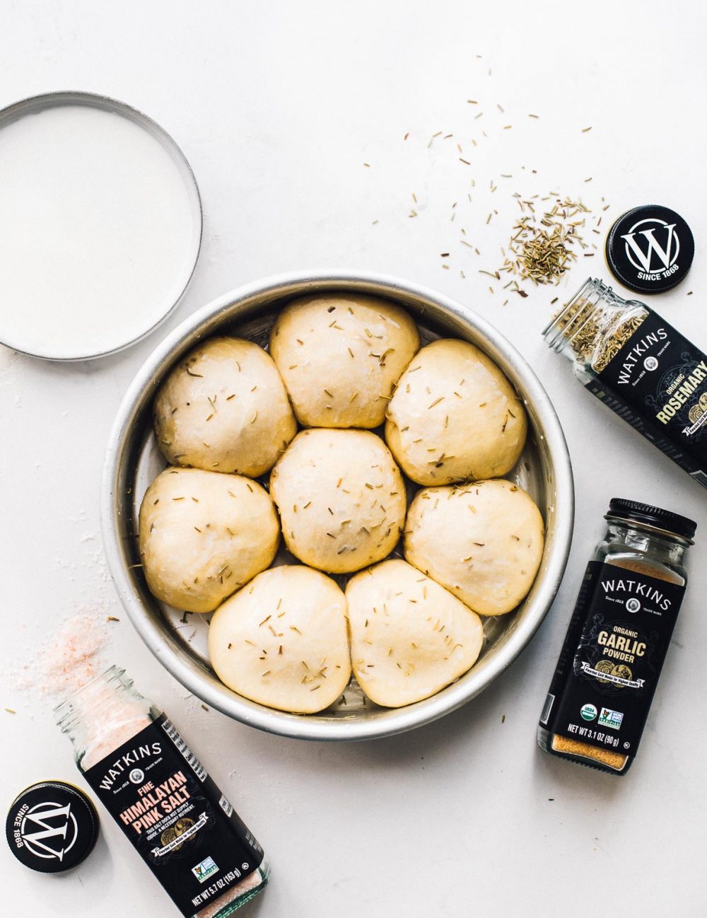 sourdough dinner rolls in a round pan with spices surrounding the pan