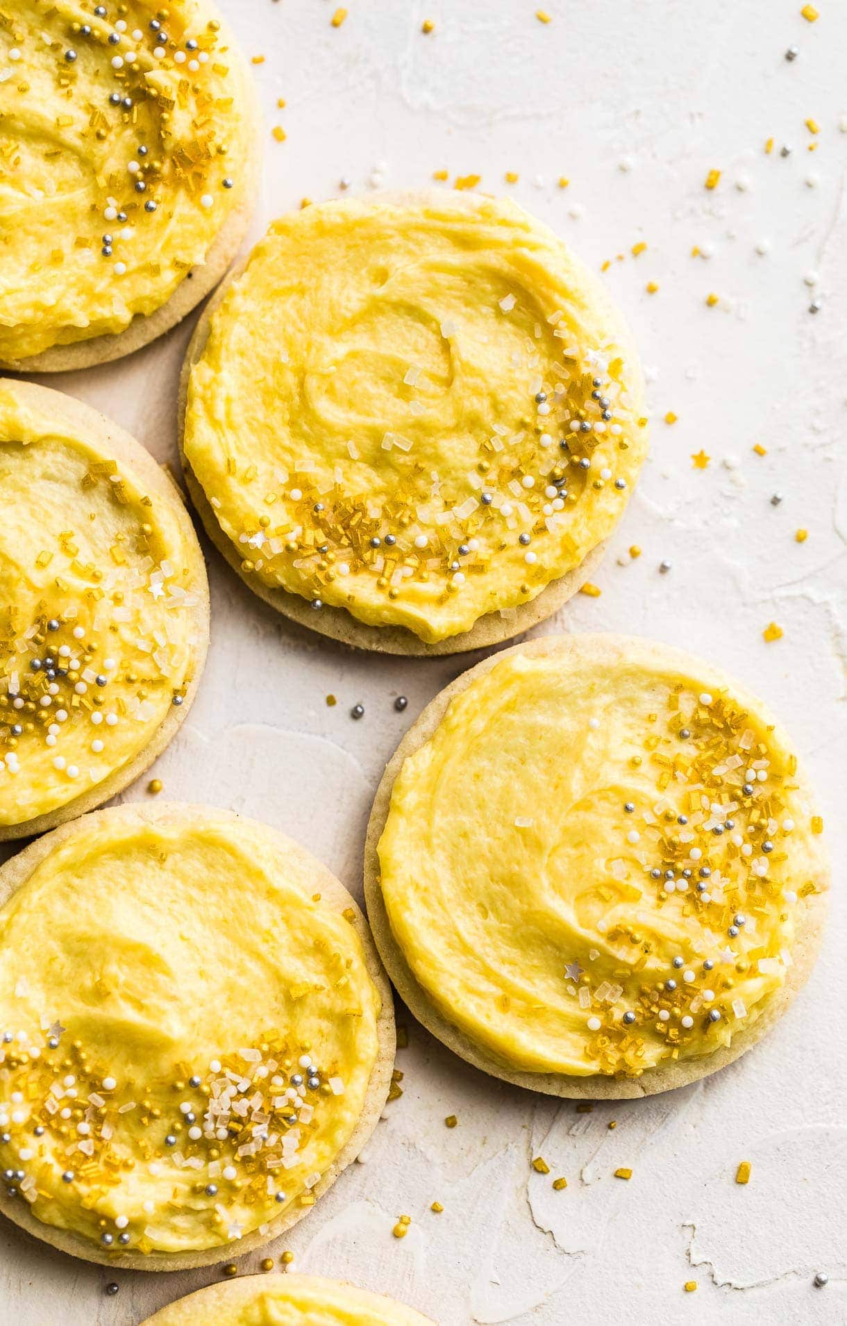 gluten free sugar cookies on a white surface, decorated with yellow buttercream frosting