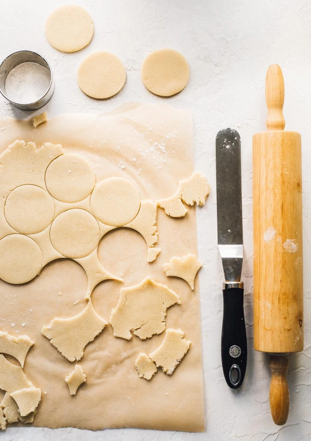 gluten free sugar cookie dough rolled, some circles cut out for cookies, with a rolling pin to the right of dough