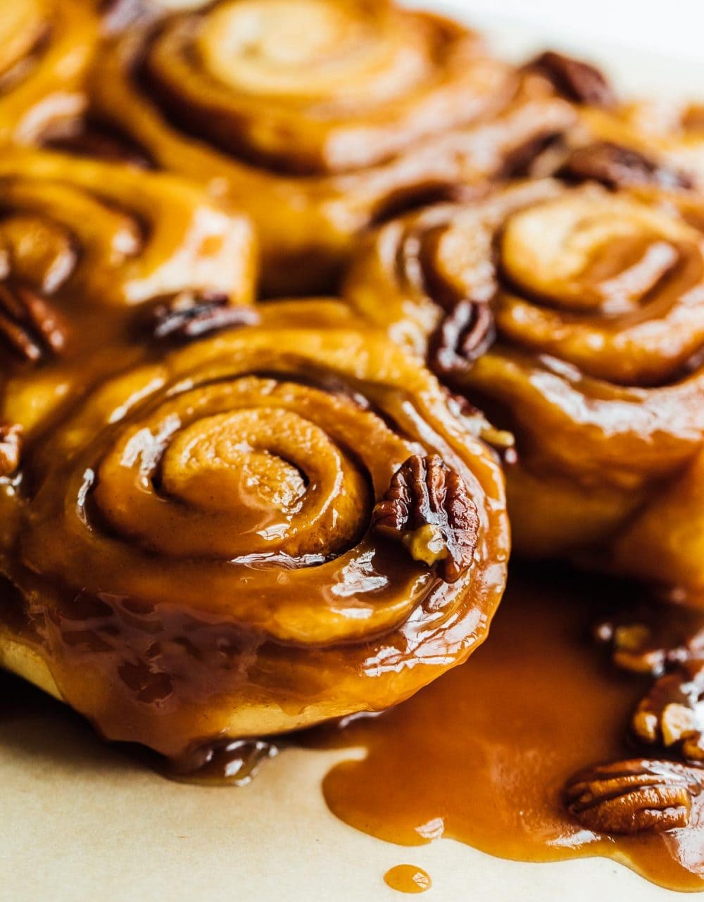Sourdough sticky buns are baked and sitting on parchment paper, caramel is surrounding them.