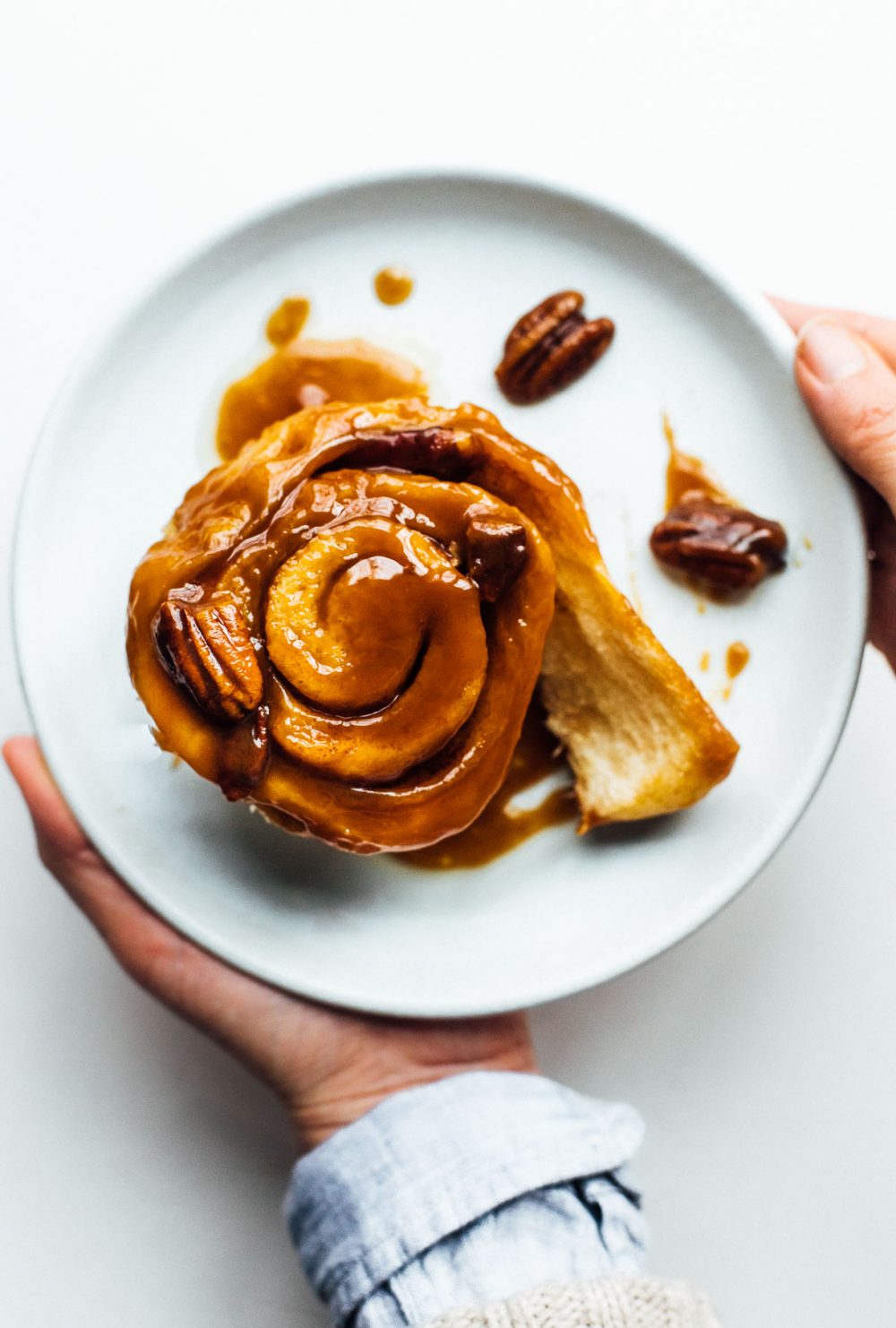 woman holding a plate with sourdough sticky bun and pecans on the plate. plate is light blue.