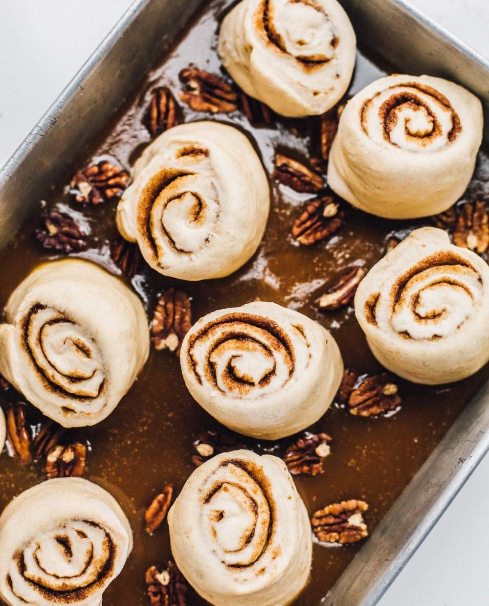 Sticky buns sitting in an aluminum pan on bed of caramel and pecans, ready to proof.