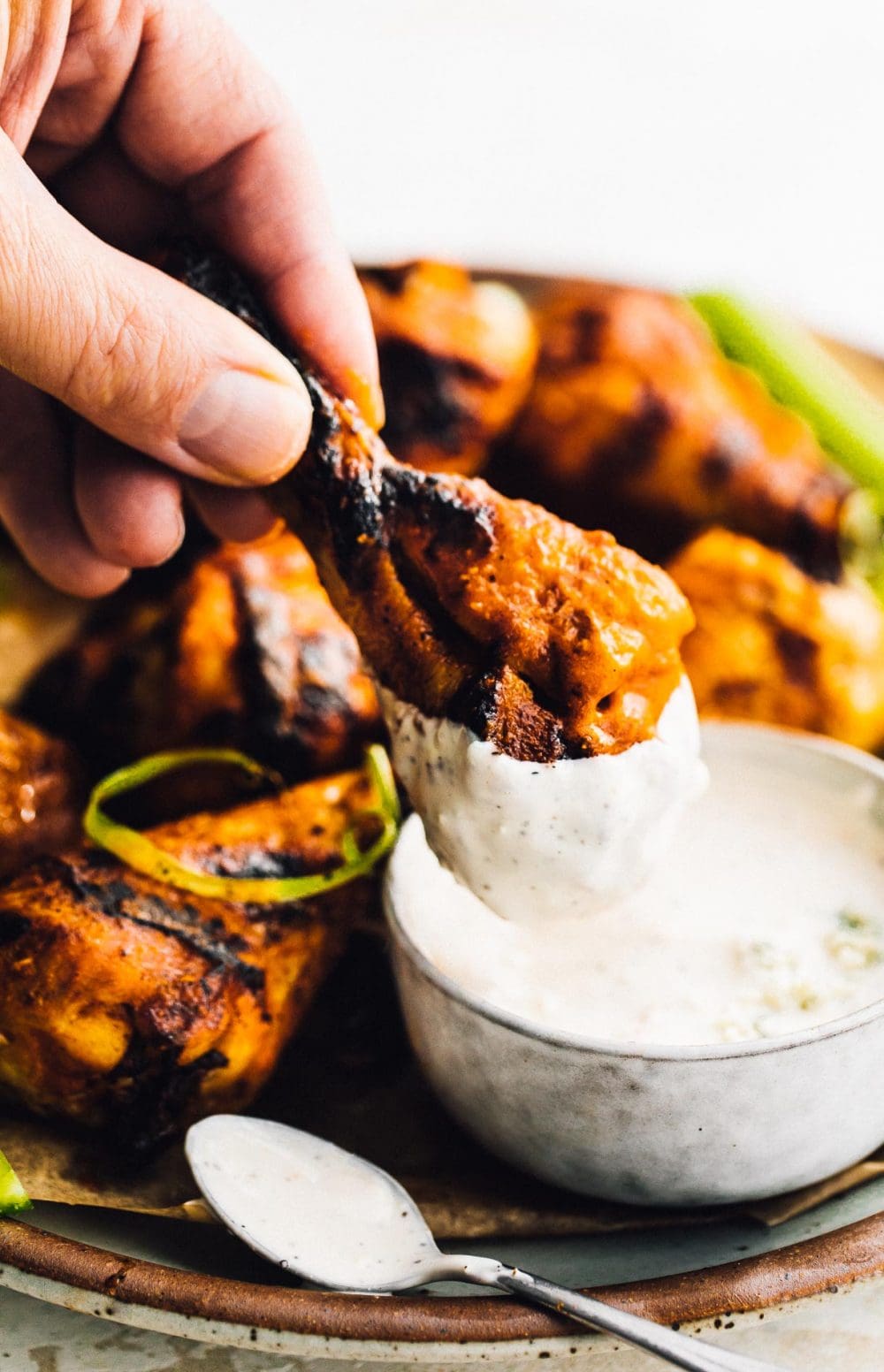 hand dipping chicken drumstick into bleu cheese dressing. 