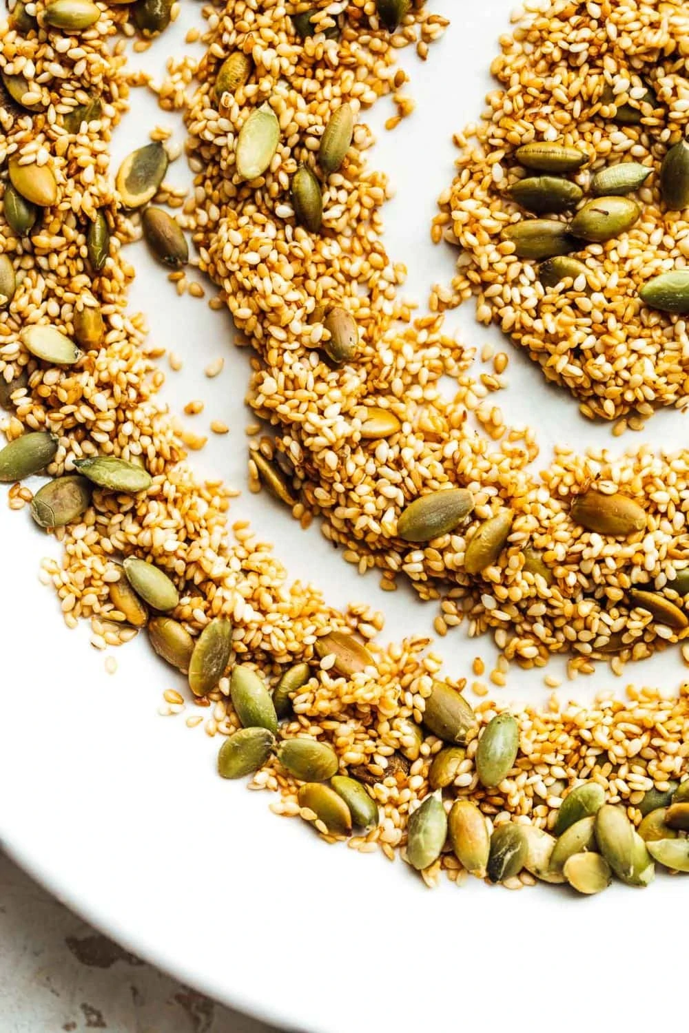 toasted sesame and pepita seeds in a swirled pattern on a white plate.