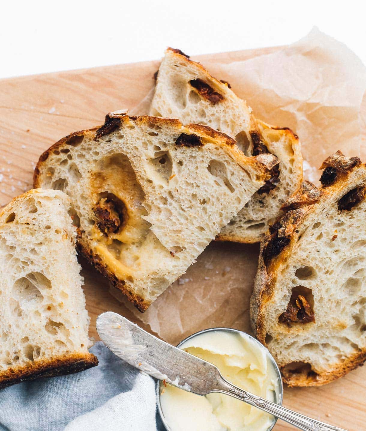 sun dried tomato and cheddar sourdough slices on a wooden cutting board, butter in a little silver dish.