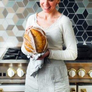 woman holding sourdough bread in front of her oven, she has a white shirt on.