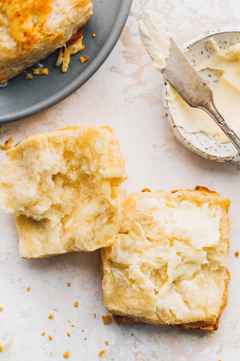 a biscuit cut open with small bowl of butter to its right