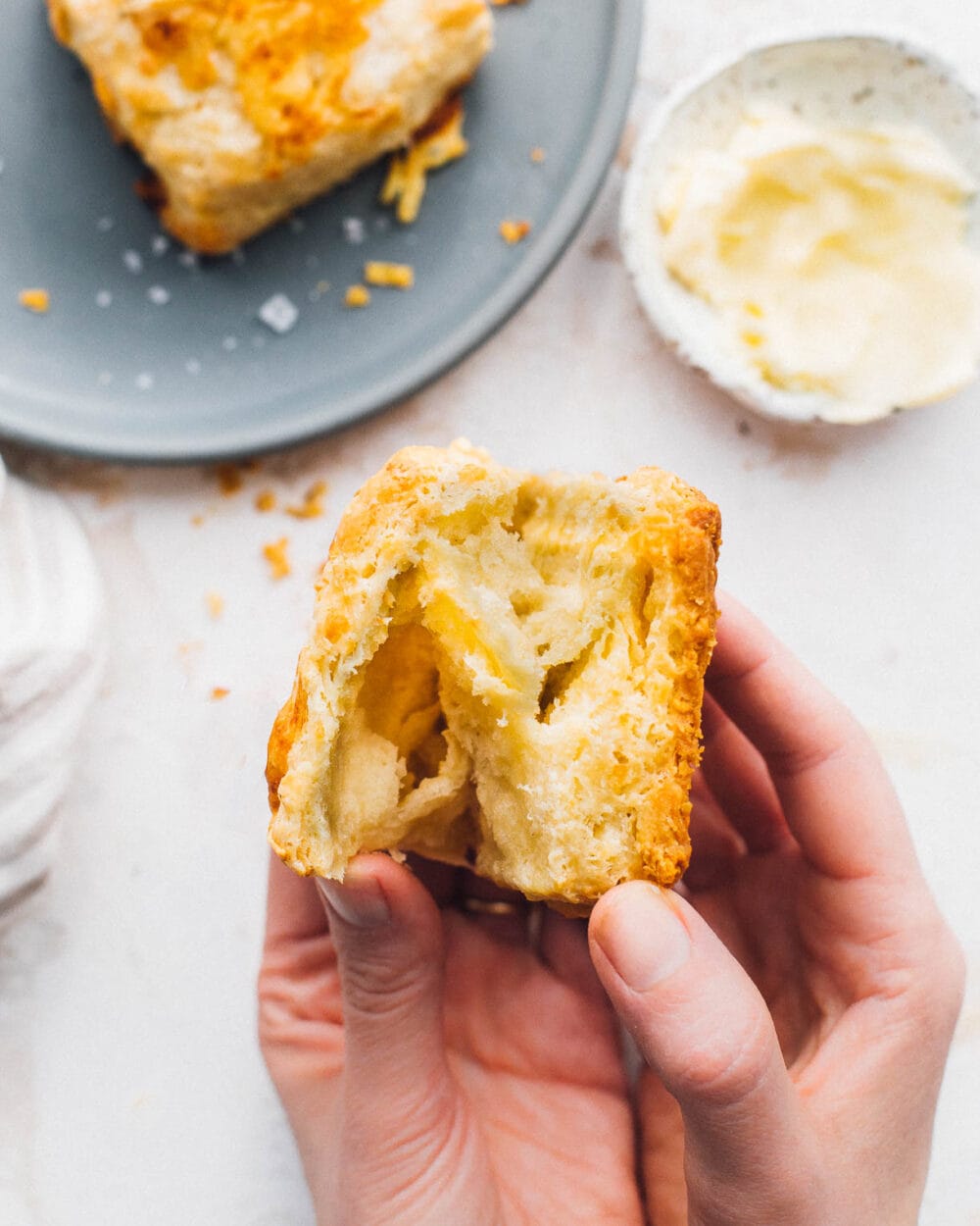 holding biscuit in hand, pulling layers apart, plate in top left of photo with another biscuit