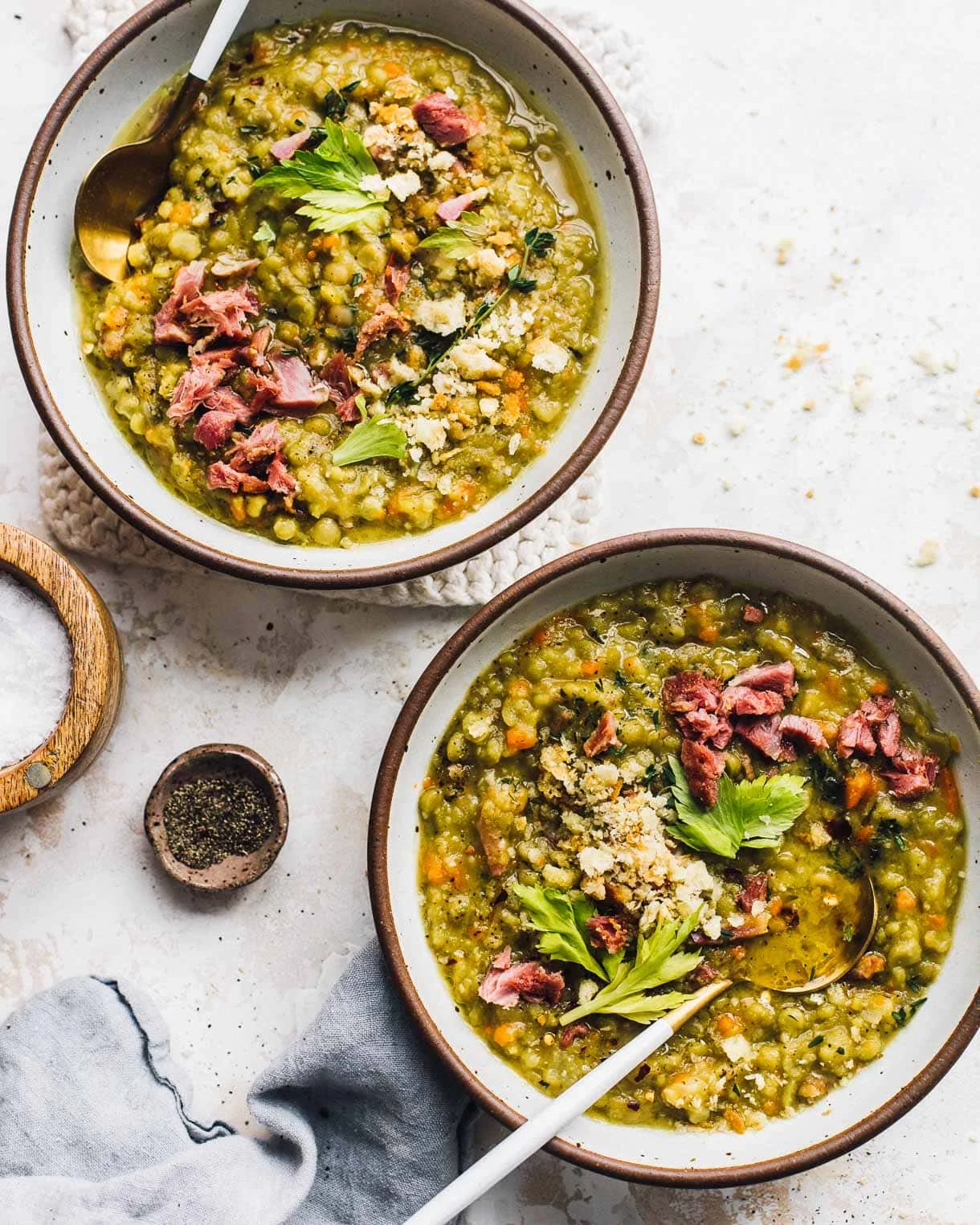 two bowls of split pea soup , with salt and pepper dishes to their left.