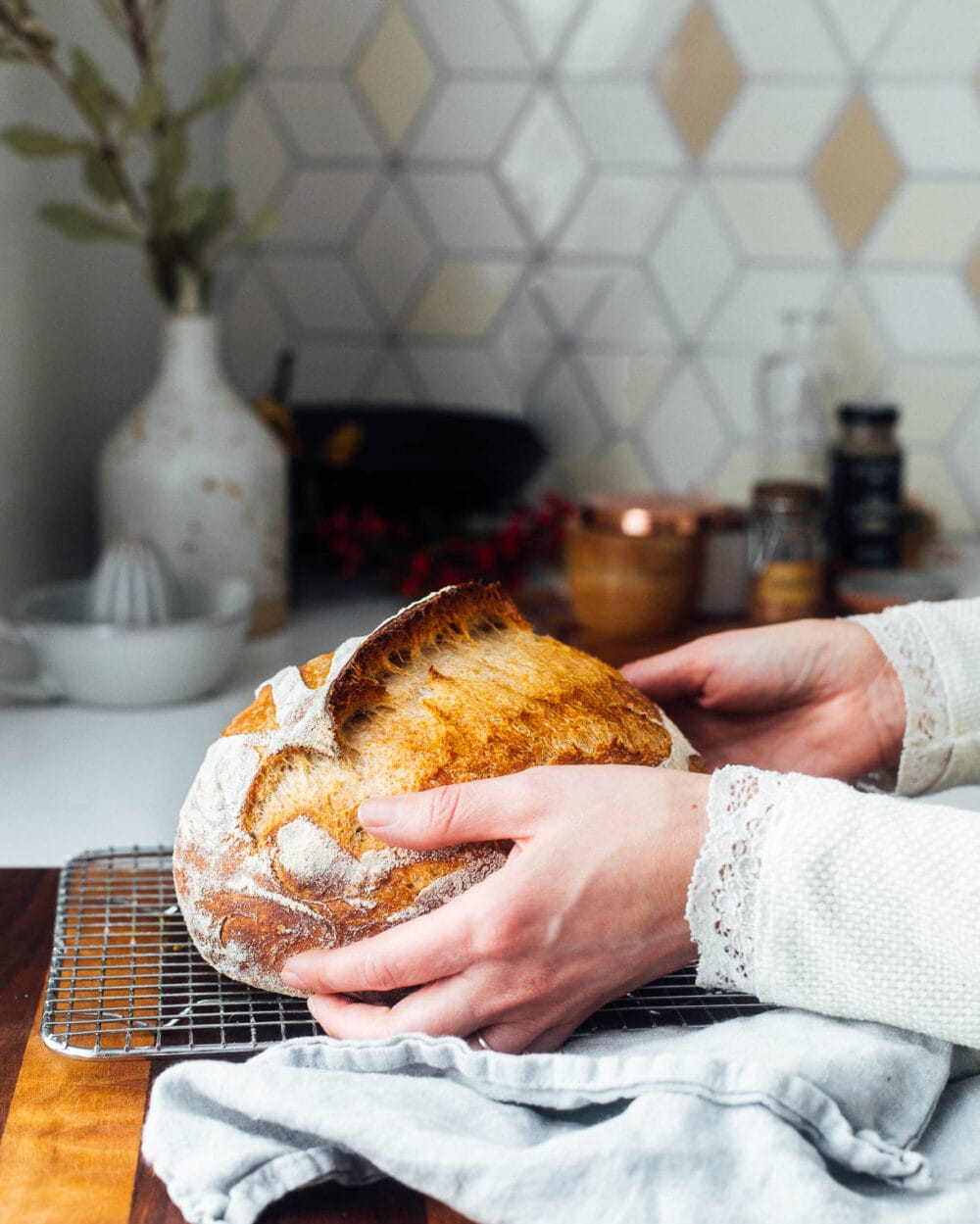 whole wheat sourdough bread being placed on a wire cooling rack, that is sitting on top of a wooden cutting board