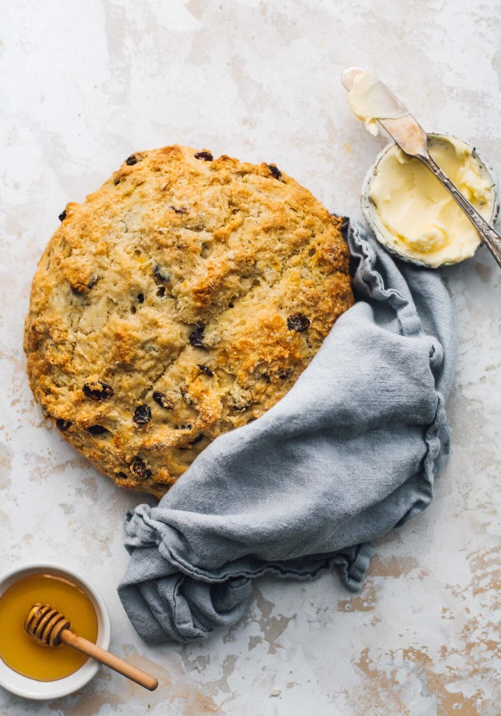 sourdough discard soda bread with a blue cloth wrapped around it, honey in a small bowl and butter in a small bowl next to it. 