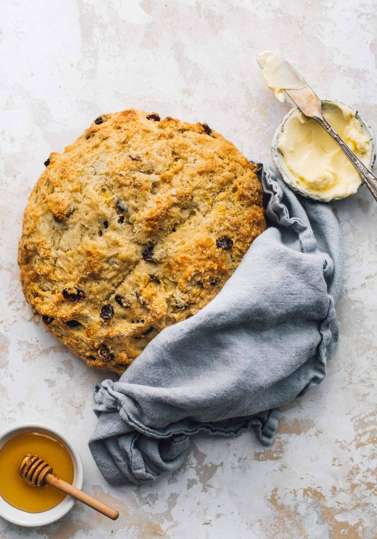 sourdough discard soda bread with a blue cloth wrapped around it, honey in a small bowl and butter in a small bowl next to it.