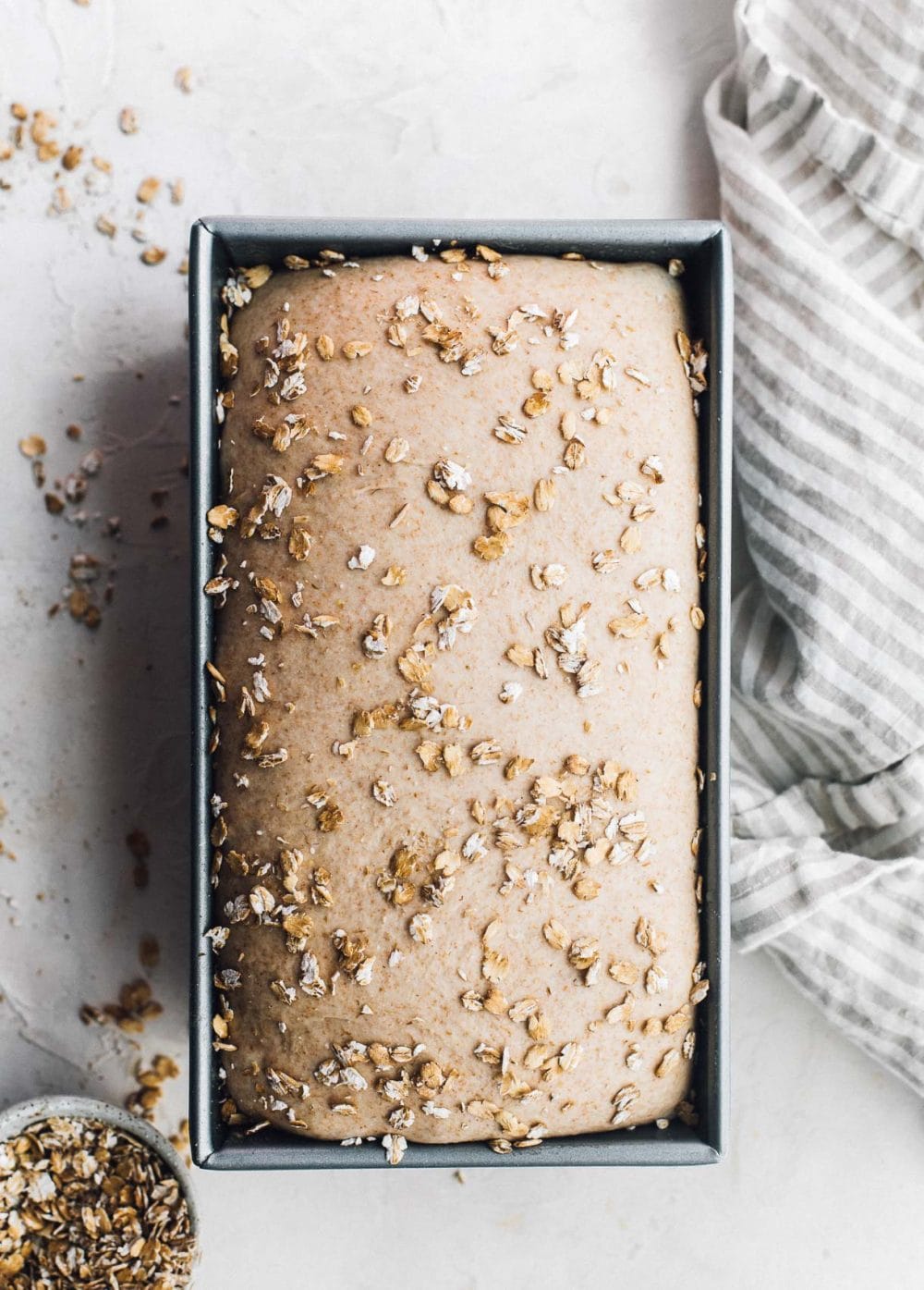 Whole wheat sandwich bread in a loaf pan with oats sprinkled on top. unbaked.