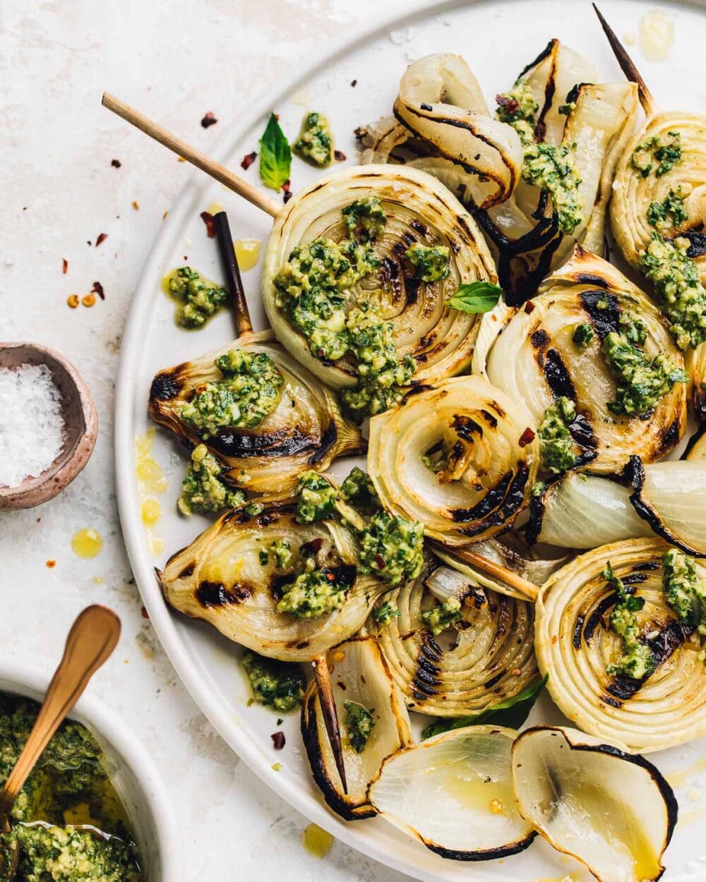 white plate holding grilled onions on skewers with pesto