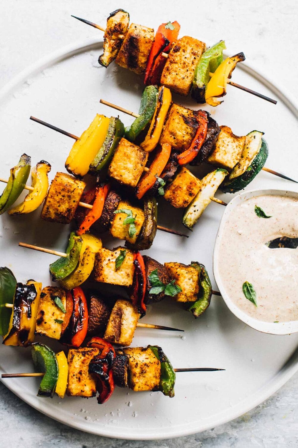 grilled veggie skewers on a white plate with dipping sauce