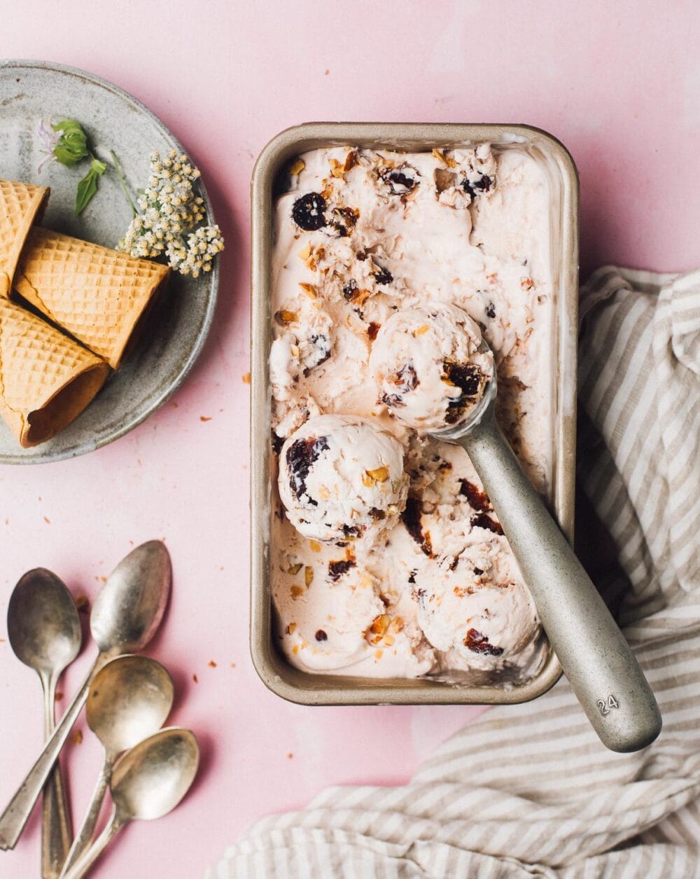 cherry nut ice cream in a loaf pan with four spoons to left of pan.