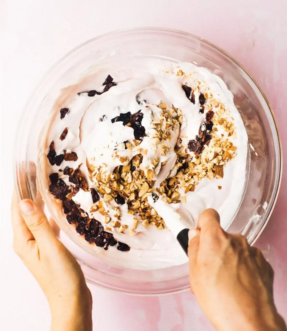 folding tart cherries and almonds into no-churn ice cream base, in a glass bowl.