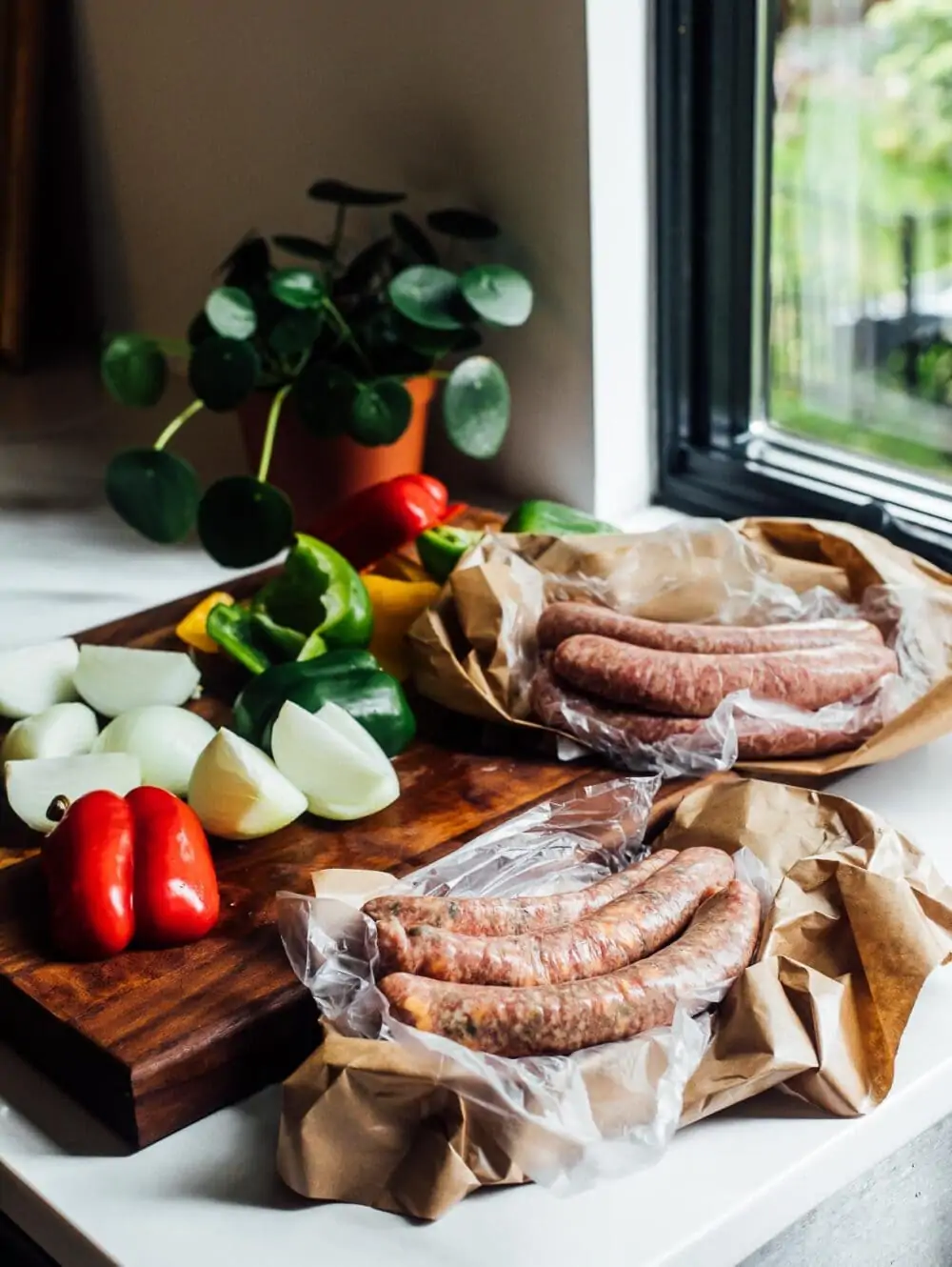 fresh brats sitting on a kitchen counter amongst a wooden cutting board with vegetables.