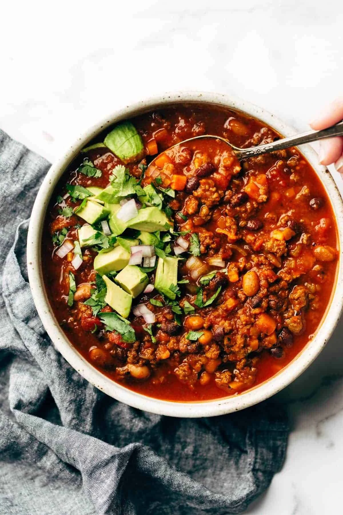 chili in a white bowl, topped with avocado and herbs