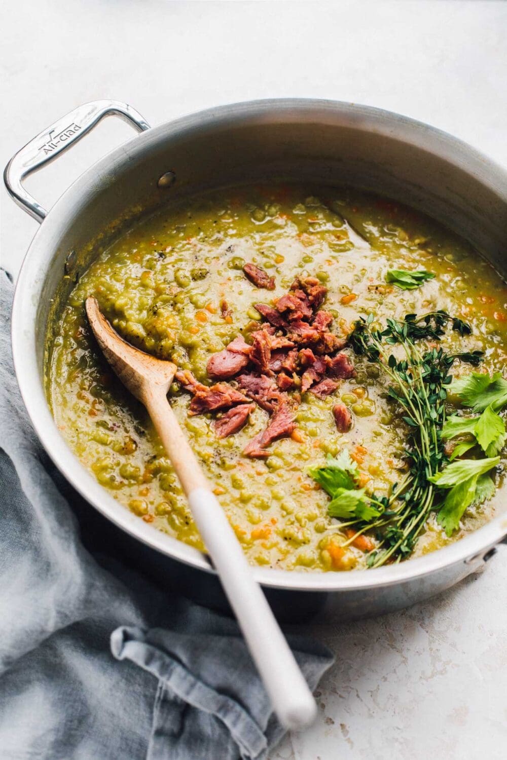 split pea soup in pot with herbs on top and wooden spoon.