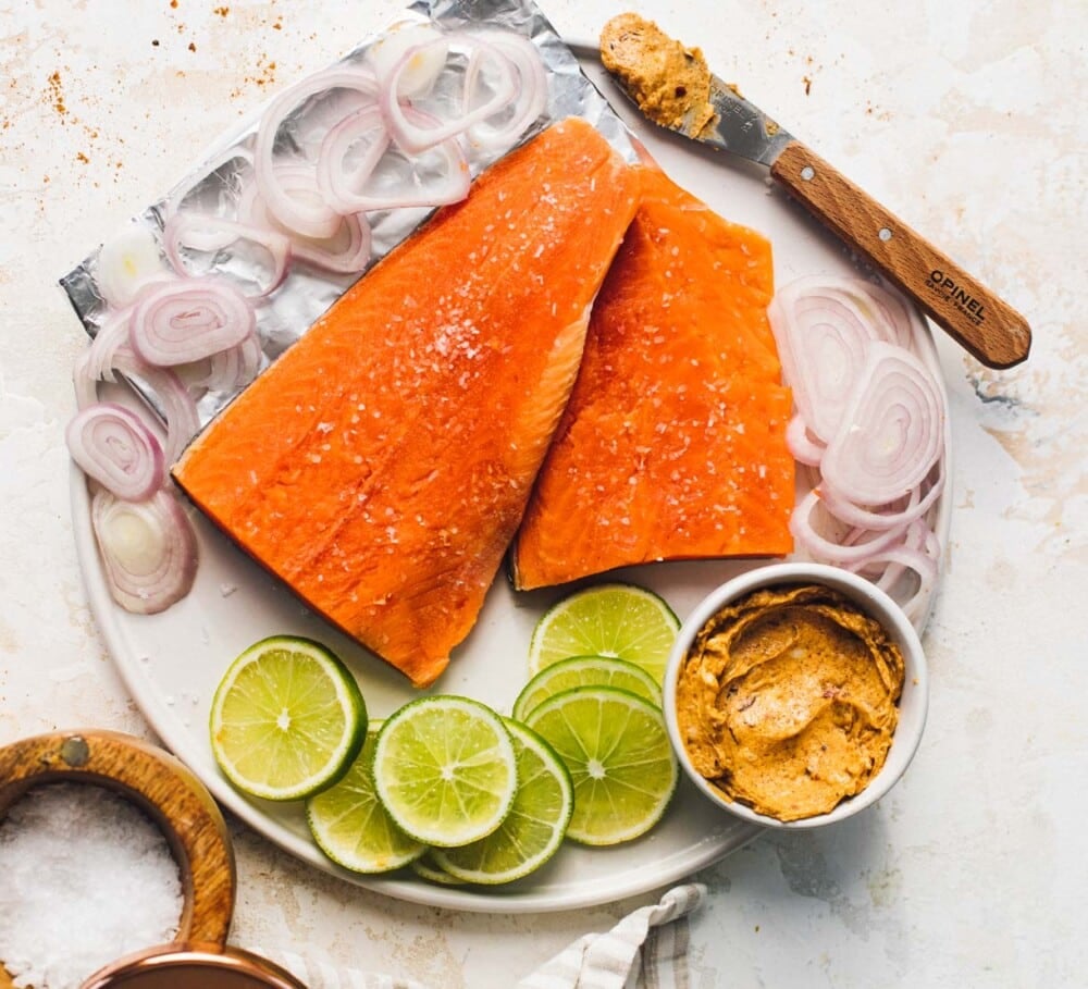 salmon filets on a white plate with lime slices and harissa butter.