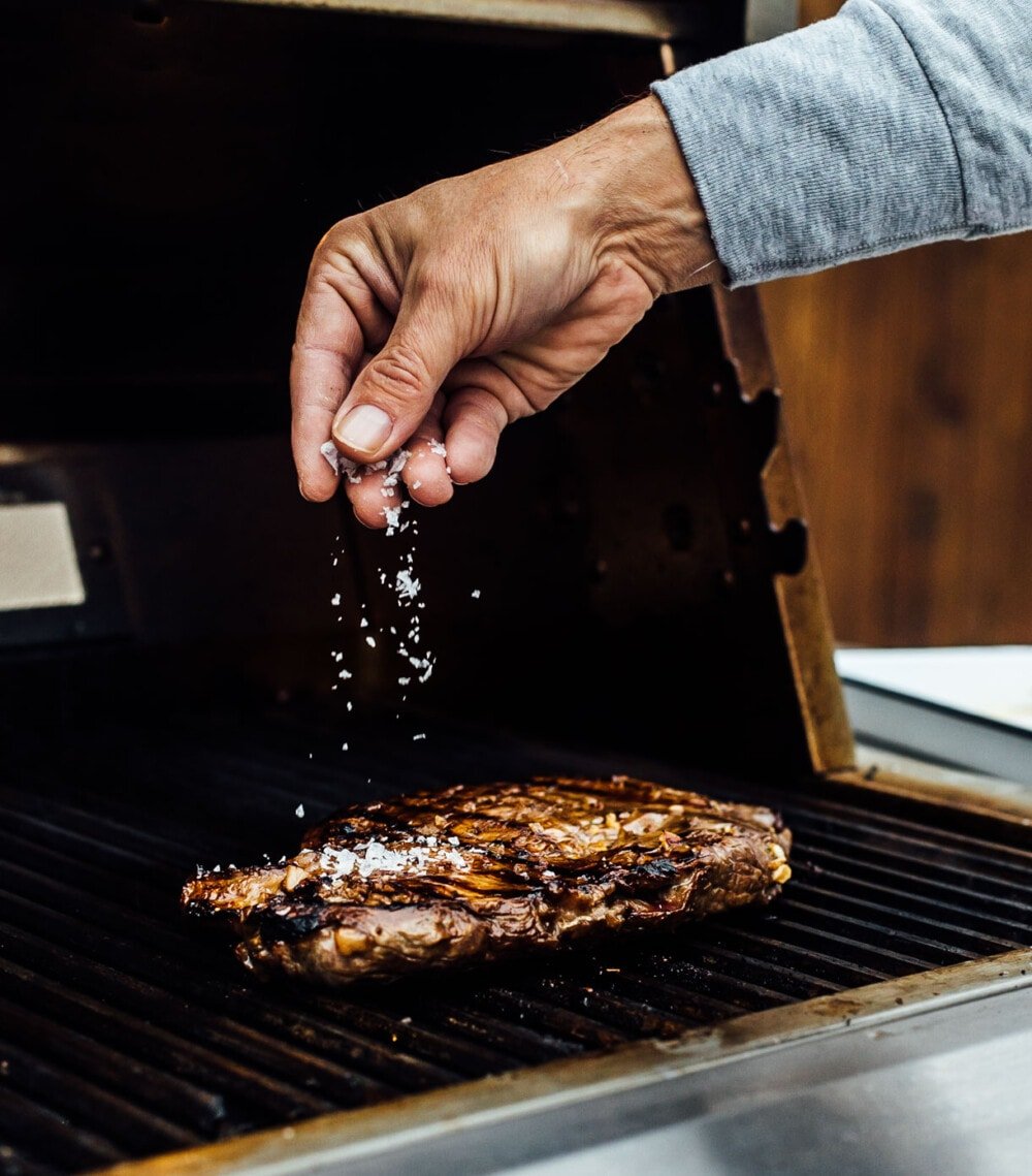 sprinkling salt on flank steak on the grill