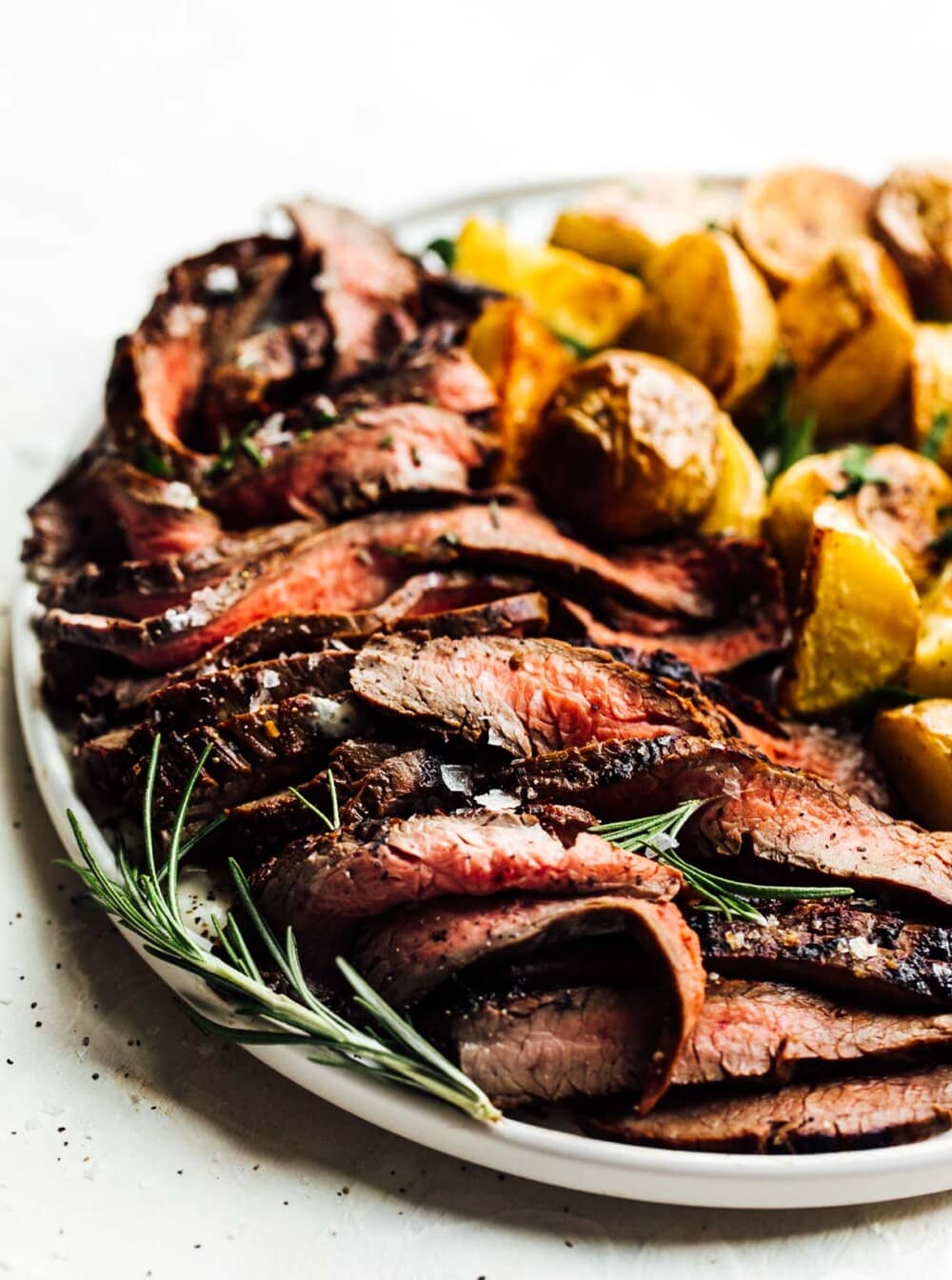 grilled flank steak with roasted potatoes on white plate