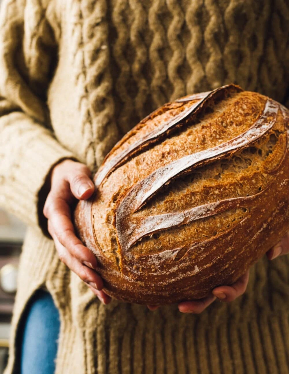 woman in sweater holding a loaf of sourdough bread