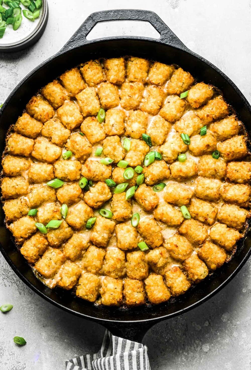 tater tot hotdish baked in a cast iron skillet with green onion garnish.
