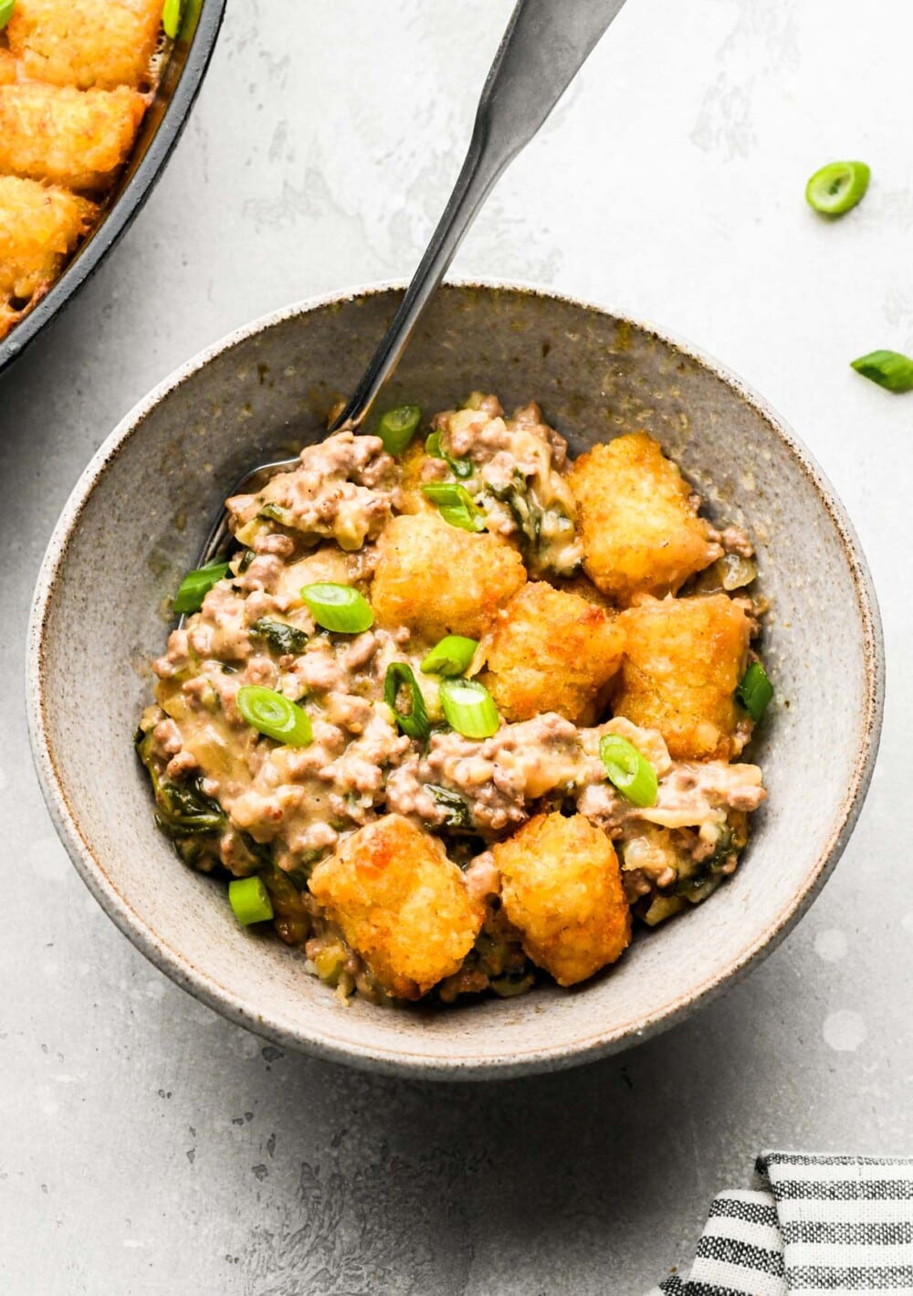 tater tot hotdish in a grey bowl with spoon.