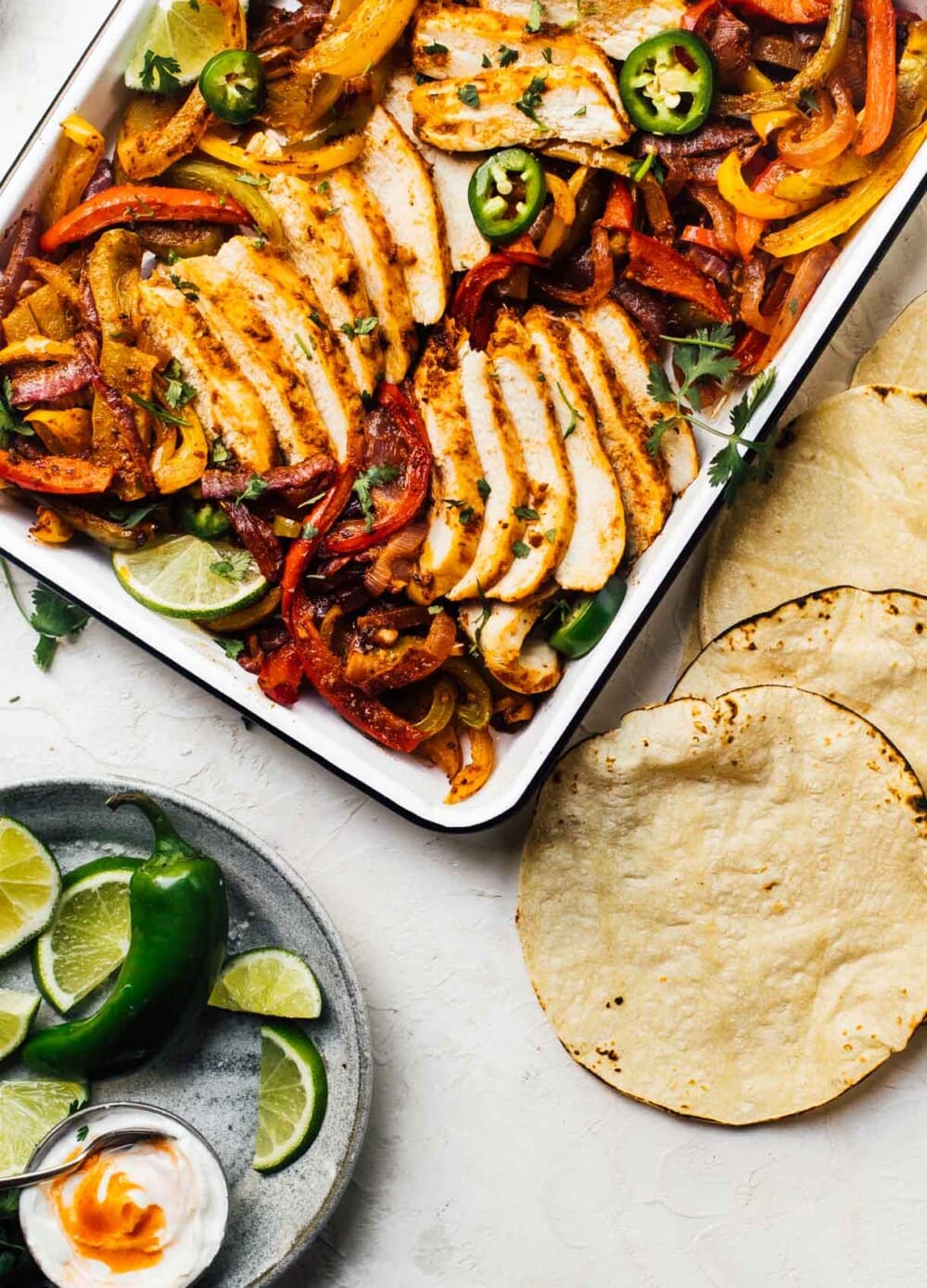 baked chicken fajitas in a white enamel pan with tortillas alongside them. 