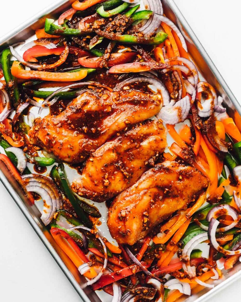 peppers and onions with chicken marinating on a sheet pan