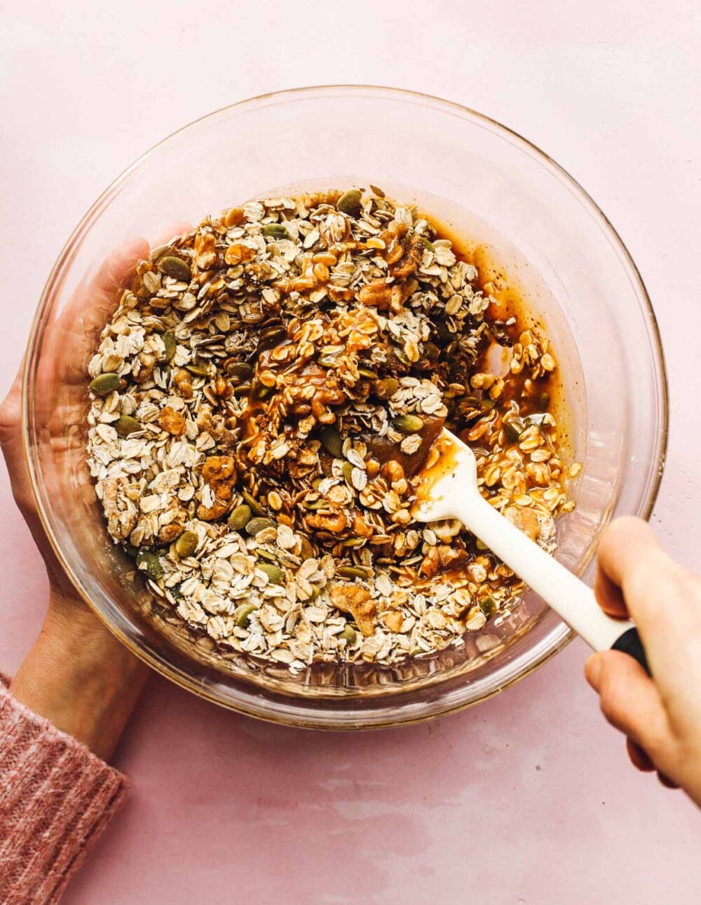 stirring granola in a clear bowl with a spatula